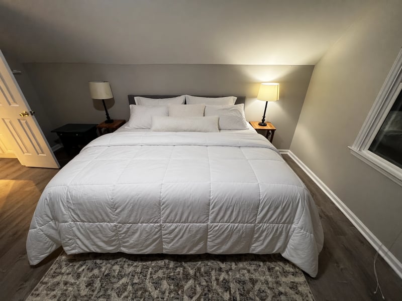 The same bedroom with the bed neatly made and pillows arranged against the gray headboard