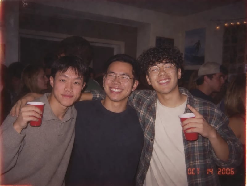 Three smiling men pose shoulder to shoulder at a crowded indoor party, the men on either side holding red cups