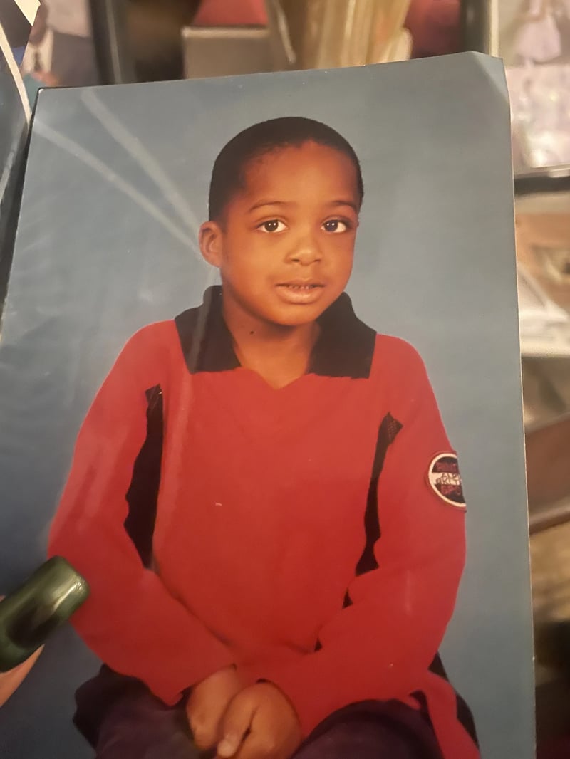 A printed studio portrait of a young child in a red shirt with a black collar against a blue background